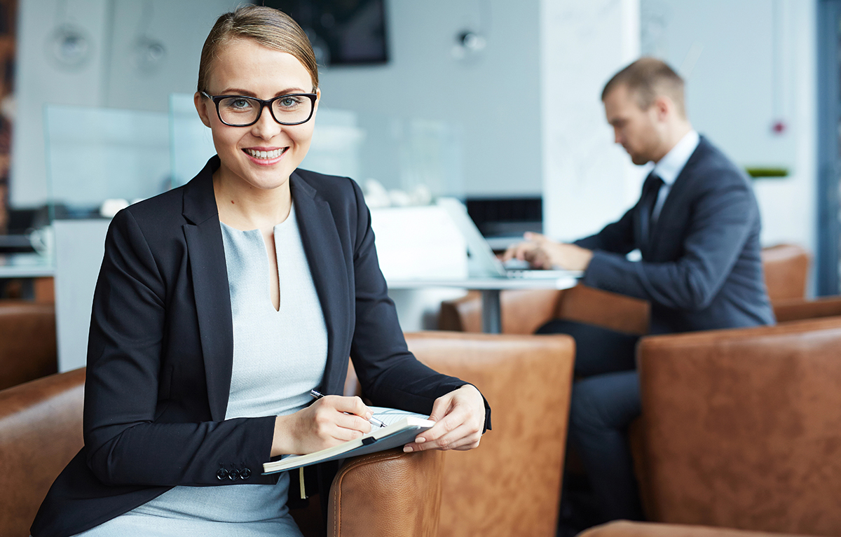 Junge Managerin macht sich in einem Sessel sitzend Notizen