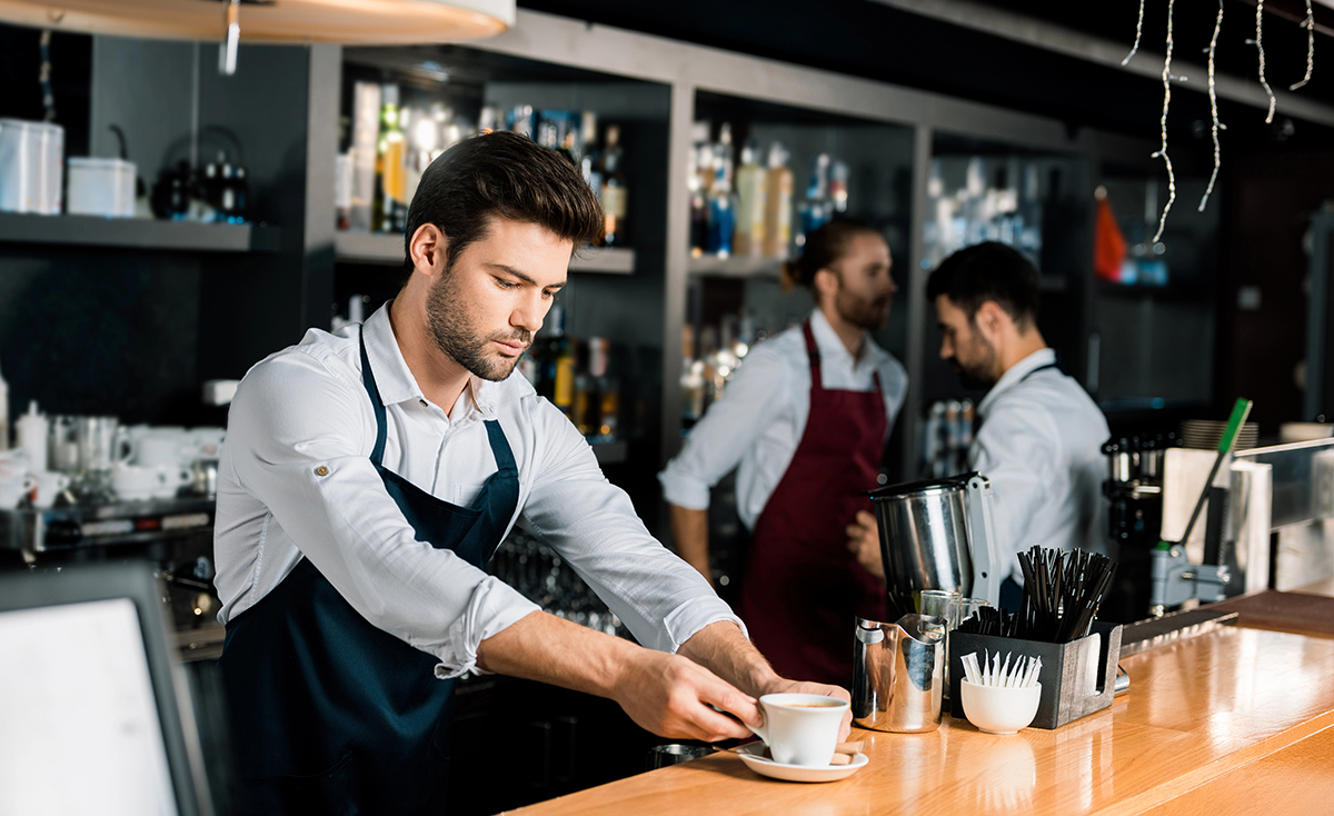 Junger Servicemitarbeiter serviert eine Tasse Kaffee am Tresen
